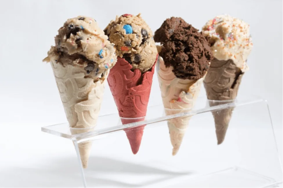 One of the best Things To Do in New York is to indulge in the latest fad - pictured here are 4 waffle ice cream cones standing in a clear perspex display stand, each with different ice cream flavours including cookie dough, chocolate chip and penut butter 