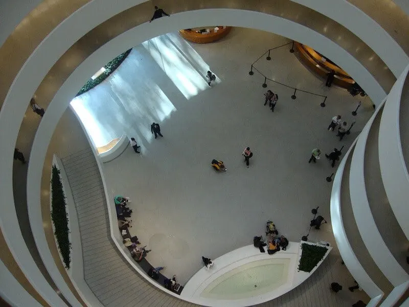 View from the top floor of the Guggenheim Museum looking down on its white concentric circle layouy with people in the atrium below