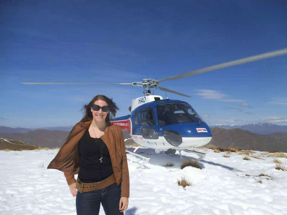 Vicki in front of a helicopter on top of a snowy mountain