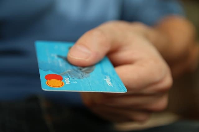 Mans hand holding a blue credit card in focus