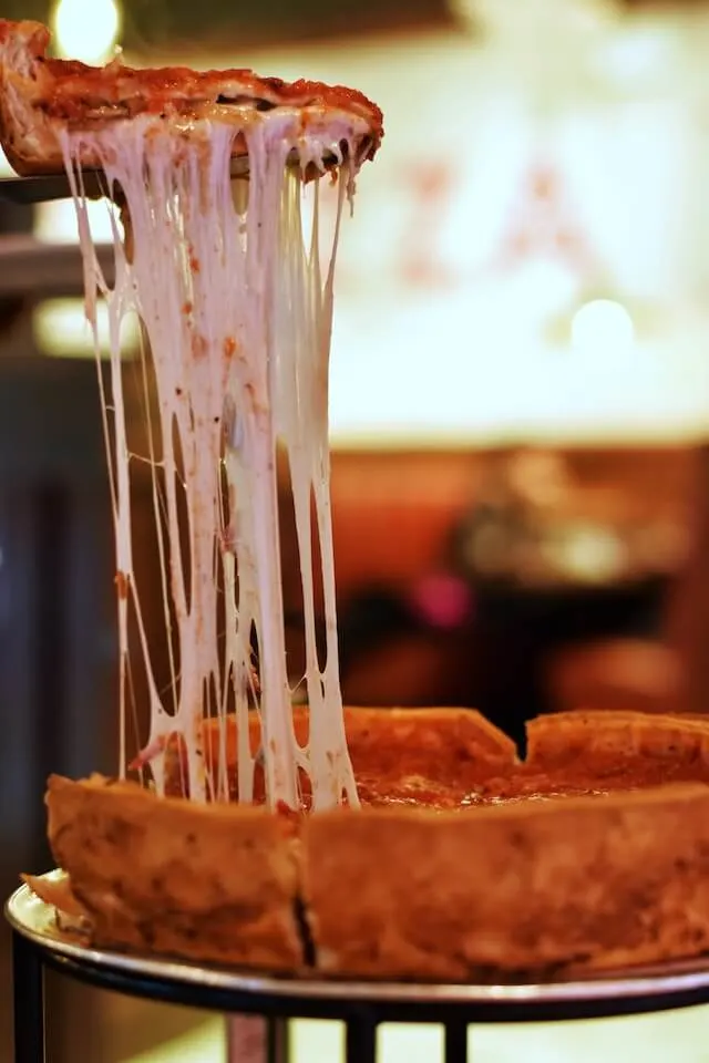 A slice of deep dish pizza being raised from the pie, the cheese stretching up from the base