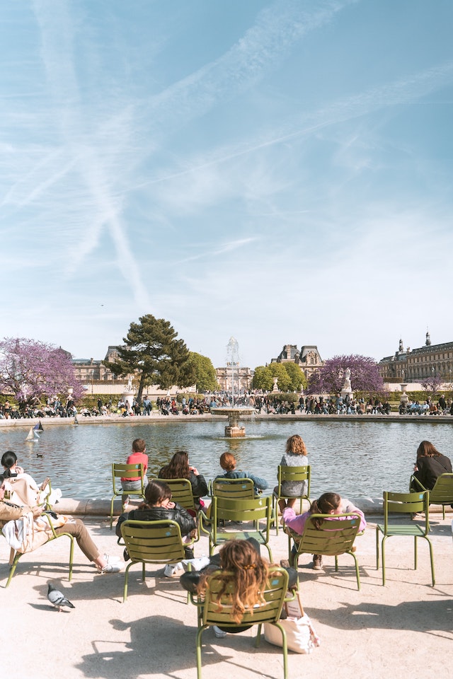 Poeople sat on green chairs next to a lake with museum buildings in the distance on Rue du Rivoli Paris