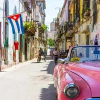 Old Pink Cadillac parked at the front right of the shot on a quite Cuban street with the Cuban flag draped from a balcony in the background