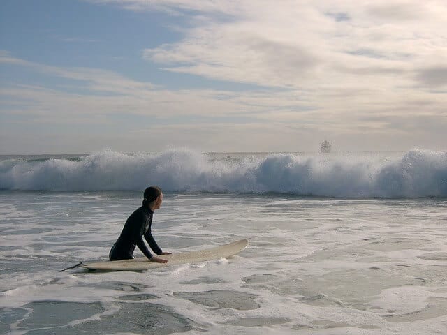 Woman holding onto a surfboard facing an oncoming wave