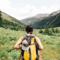 Eco Friendly Gifts for Travel - female traveler looking out across a green field wearing a backpack