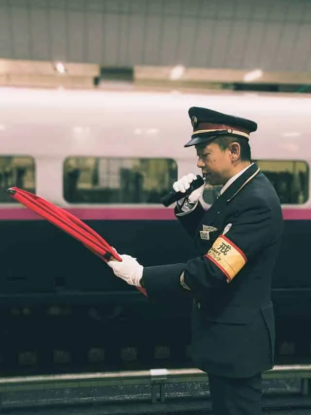Conductor at Tokyo Train Station announcing the approaching train with a red clipboard