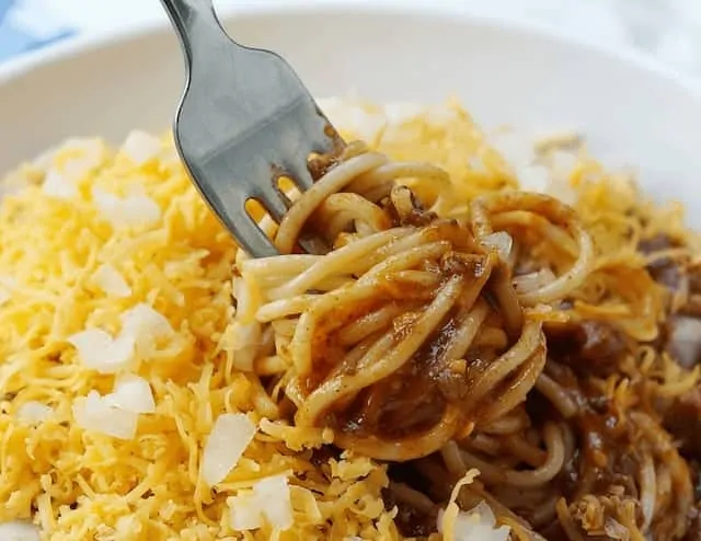 Cincinatti Chilli - spaghetti covered in mince, shredded cheese and onions with a fork twirling the spaghetti
