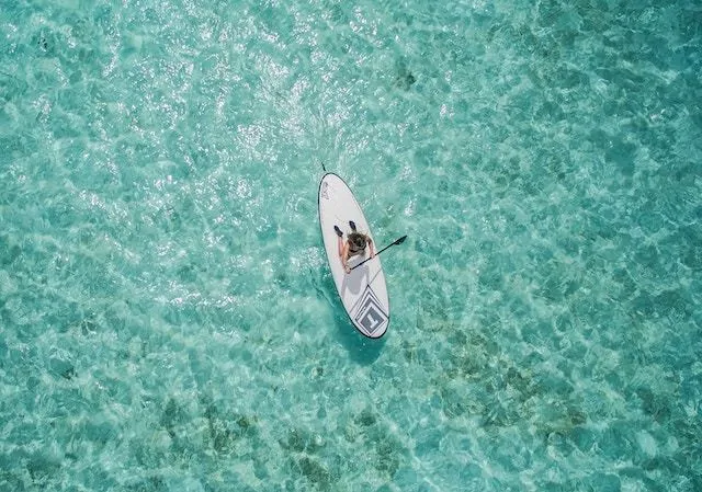 Woman kneing on a stand up paddleboard holding a black paddle surrounded by clear blue water