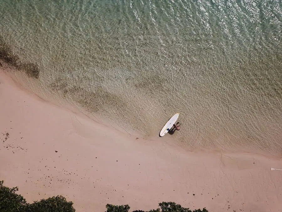 Top down aerial shot of a paddleboard at the waters edge next to pink sand
