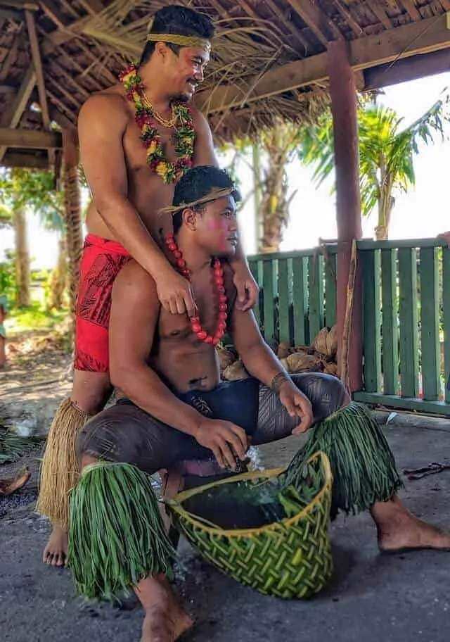 Two men dressed in traditional Samoan outfits, one whose body has the male traditional tatoo