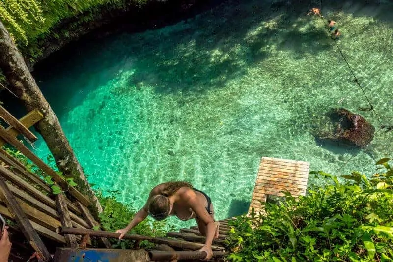 To Sua Ocean Trench from above with woman climbing down the wooden ladder in a bikini