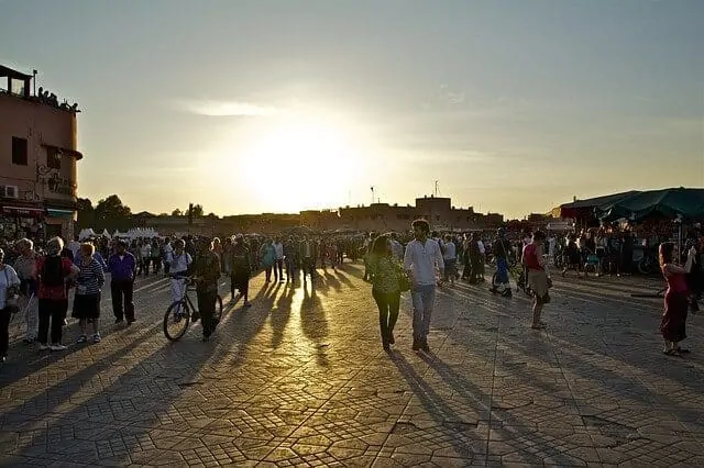 Jemaa el fna at dusk with the sun setting behind people walking towards the camera