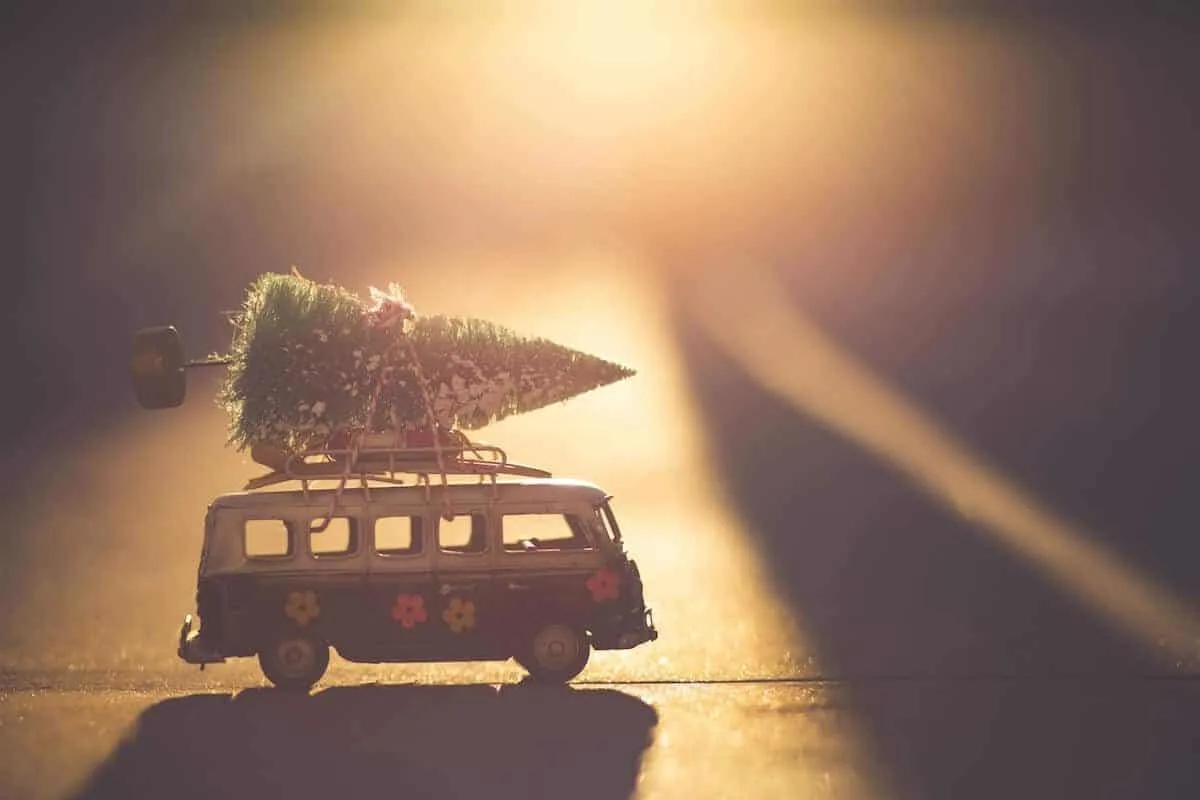 Cover photo of the best white elephant gifts for travel lovers featuring a mini vw campervan with a christmas tree on top bathed in a golden light from a sun set at the back of the shot