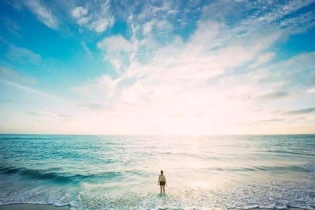 Kogalla Beach just before sunset, with a woman standing in the ocean with her back to the camera and the sky is shades of blue with bright light flares