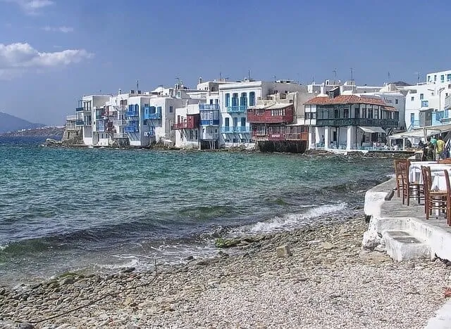 Colourful building line the ocean wall in the distance; in the foreground is a shingle beach with the waves lapping gently on the shore