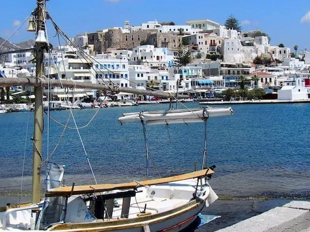 Small finishng boat moored at the forfront of the image, the ocean is behind and in the distance several multistorey buildings line the ocean wall and spread upwards onto the hill behind