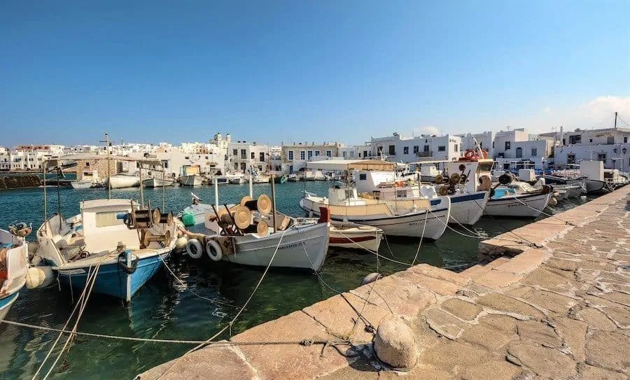 small fishing boats tied up along the harbour wall of Paros Naxos with the water behind stretching to the buildings on the shore on the other side of the marina