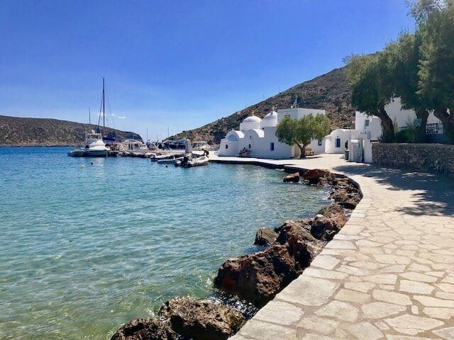 A curved path winds around the rocky shore with white single storey houses along the path in Sifnos