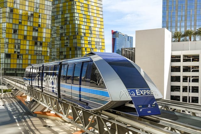 Aria Express Free Tram on the tracks in front of a yellow and silver tall building in Las Vegas