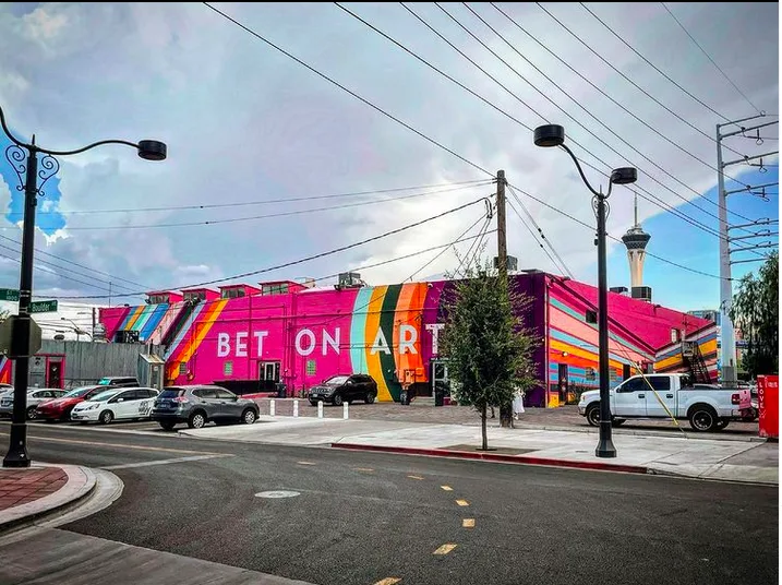 Colourful facade of the Arts Factory Las Vegas from the opposite street corner, with huge white letters on the side saying 'Bet on Art'