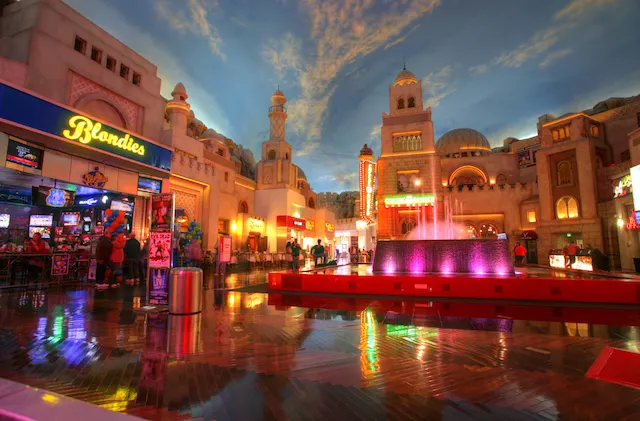 Miracle Mile row of shops indoor under a painted blue sky with white clouds, a waterfall lit up to the right