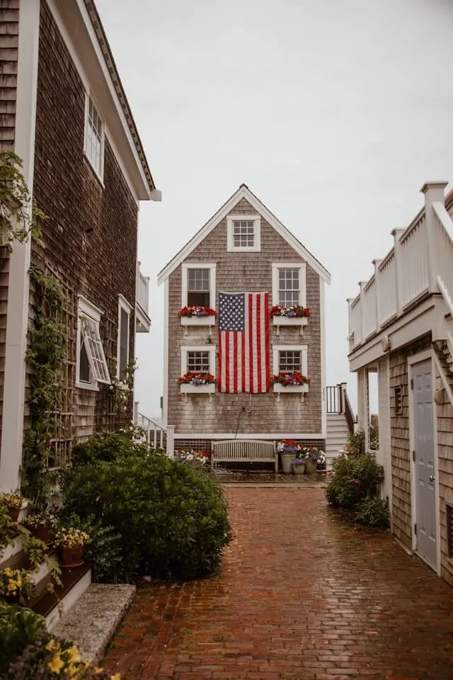 Provincetown period 3 storey double fronted house with an American flag hanging down the centre of the brick property with windows on either side 