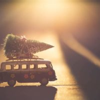 The Best Secret Santa Gifts for Travel Lovers Cover photo of a mini VW van with a Christmass tree on top driving across the sunset
