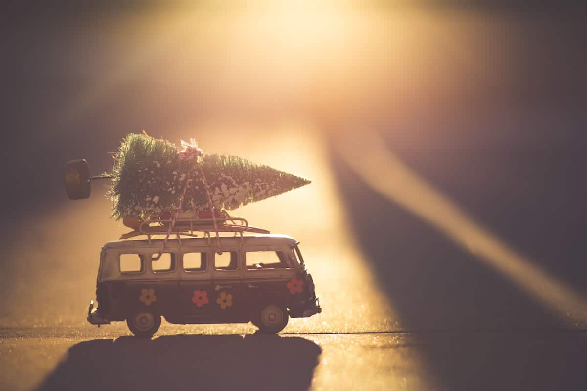 The Best Secret Santa Gifts for Travel Lovers Cover photo of a mini VW van with a Christmass tree on top driving across the sunset