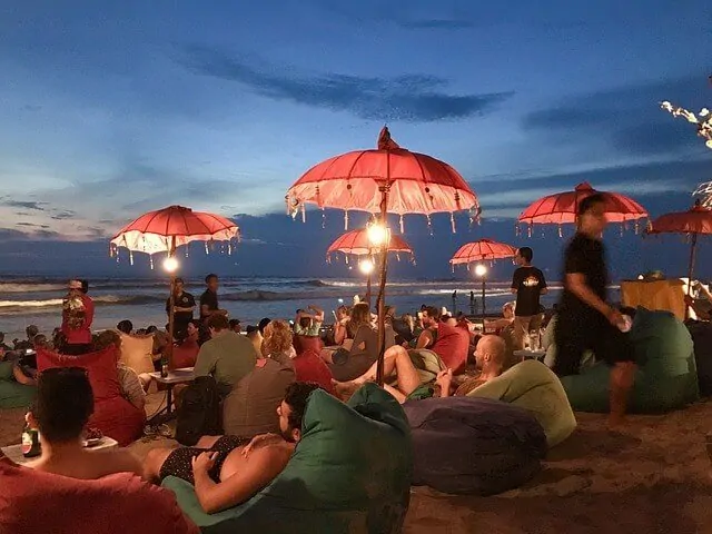 People sat on beanbags on the beach at dusk underneath gypsy umberellas lit by fairy lights