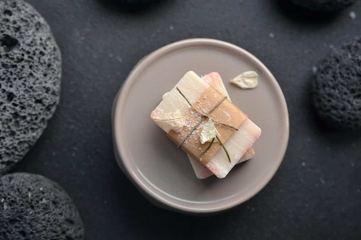 Solid Toiletries Cover Photo of Bar of soap wrapped in paper on a rose pink plate on a black table