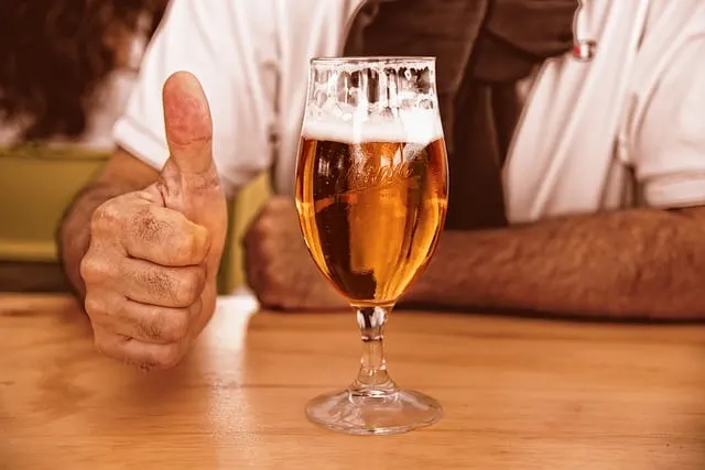 Glass of beer in front of a man with a white shirt with his thumb up