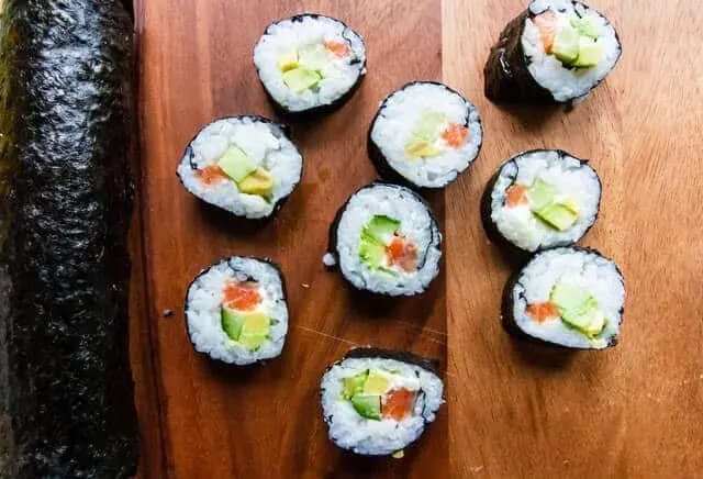 Full Hosomaki Sushi roll on the left with sliced sushi roll pieces laid out on a wooden board to the right