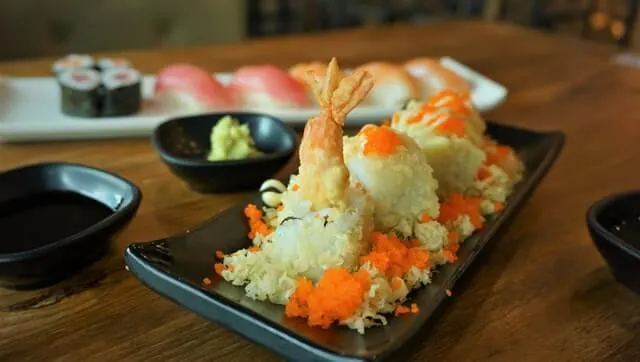 Shrimp Tempura Sushi Roll on a plate with other types of sushi behind it along with a pout of wasabi