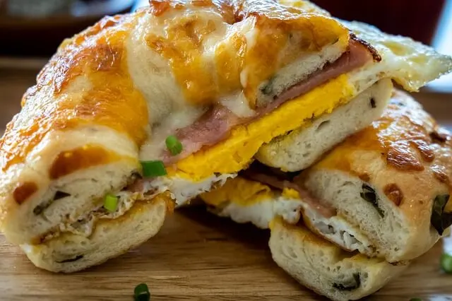 A bagel with ham and cheese cut in half and stacked on a wooden board