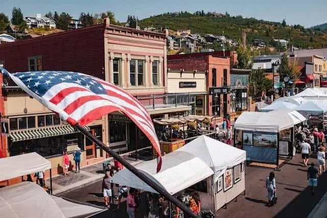 Aerial view of Park Citys Main Street featuring an aerial view of main street in Park City in summer with an American flag in the foreground and white tents of the market lining the street