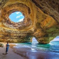 The BEST Explore Quotes to Fuel Your Wanderlust cover photo of a man standing in an ocean cave underneath a natural hole showing the shy