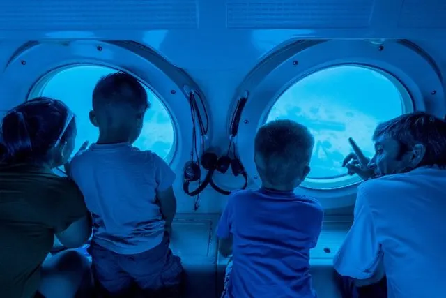 Family looking out of two porthole windows in the Atlantis Submarine Maui