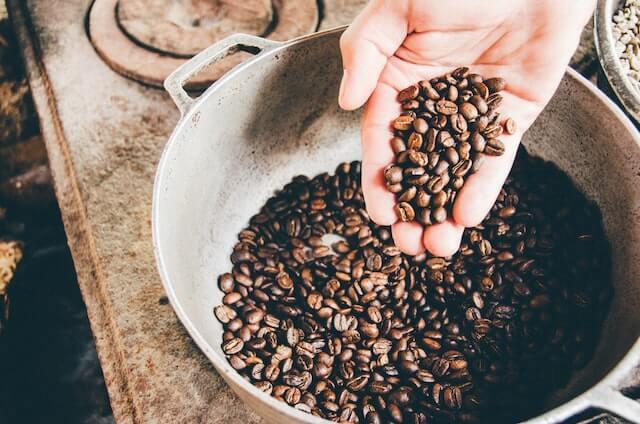 Hand holding coffee beans above a metal bowl of coffee beans