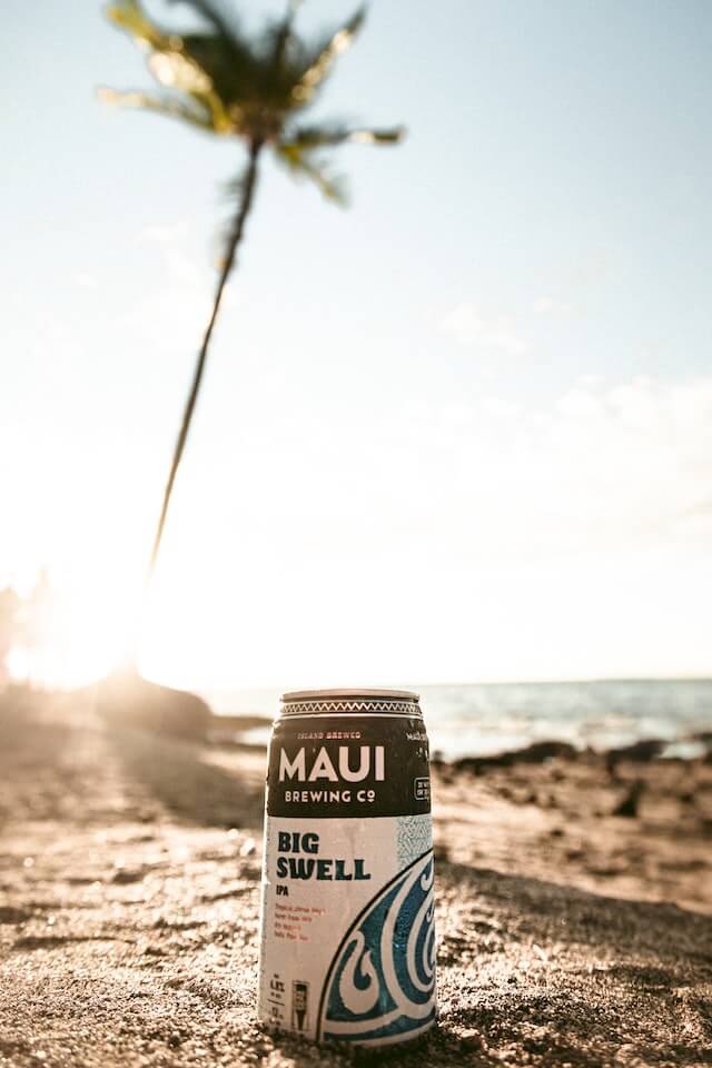 Maui Brewing Co Can on the beach with a palm tree in the background