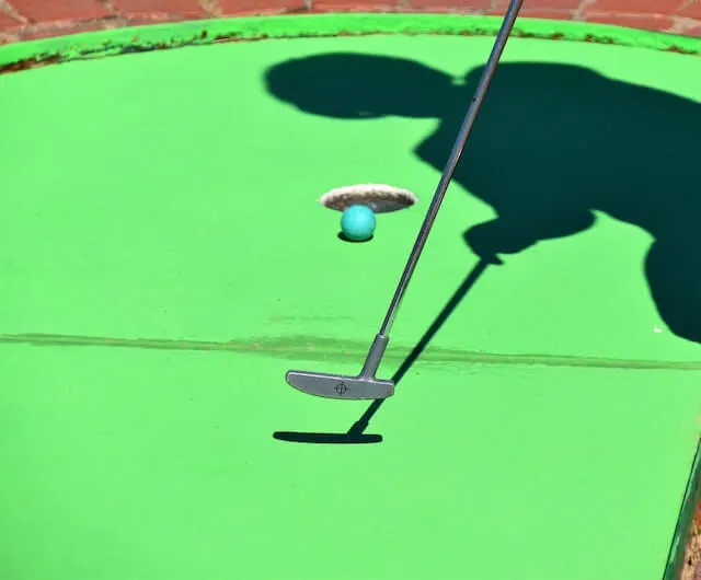 Mini Golf hole, the shadow of a child using a small putter to put a green golf ball