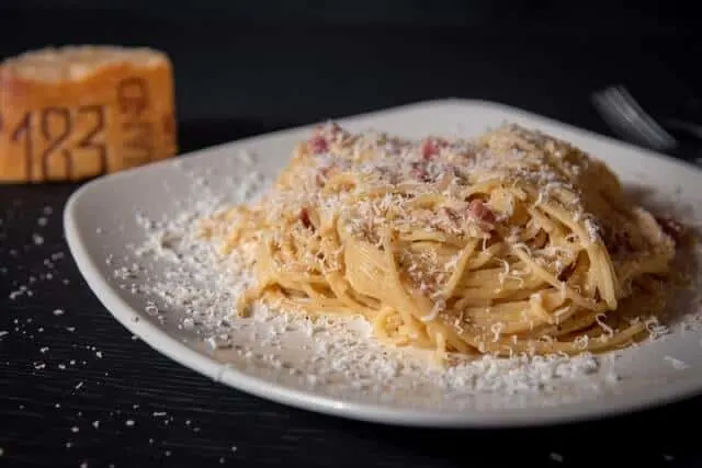 Spaghetti Carbonara on a white plate covered in parmesan cheese on a black table cloth in Rome