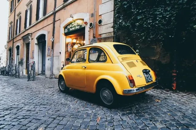 Yellow Fiat 500 parked on a cobbled street next to a restaurant in Rome