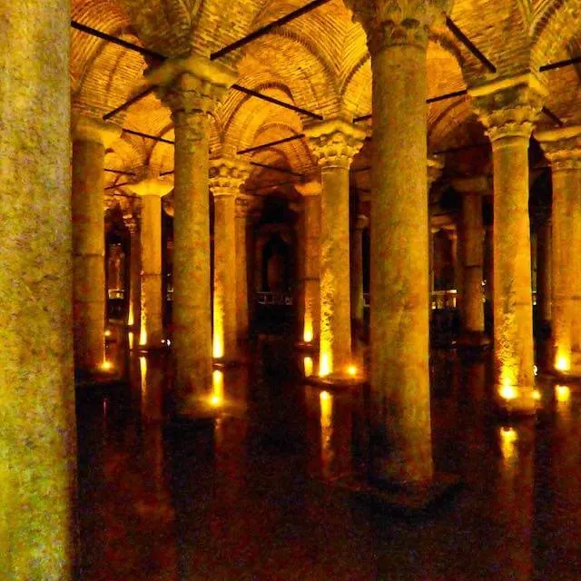 Columns equidistent apart in a grid formation supporting domed roof sections sitting in a body of water, with each column is uplit by a spotlight