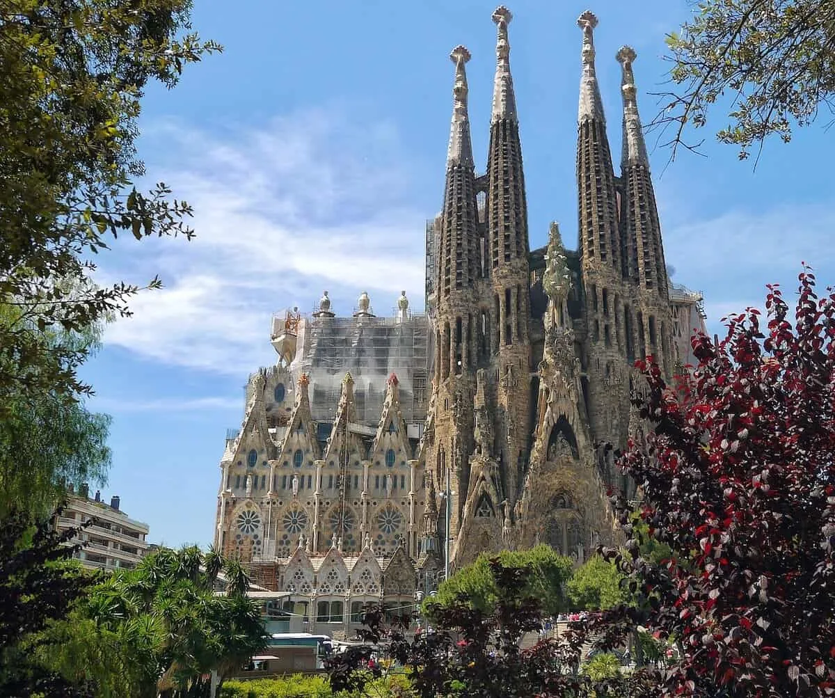 Best Places to Visit in Barcelona header image of the Sagrada Familia framed by tress from the park opposite and backed by a blue sky