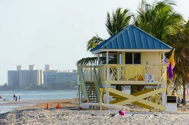 Large yellow elevated wooden hut on the beach with palm trees behind it in Biscane Bay Florida