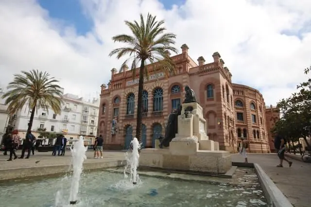 Stunning red facade of a building with a water feature and a plam tree in front in Cadiz Spain