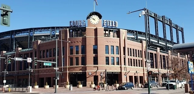 Cured facade of Coors Field Stadium with Coor and Field spelled out either side of a giant clock on top of the building under a clear blue sky