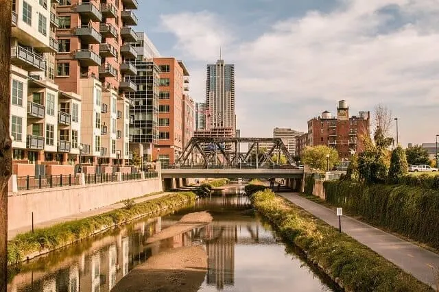 The River in Downtown Denver with a footpath running alongside the right side of the water and high rise apartments on the left with a metal industrial styled bride crossing the water