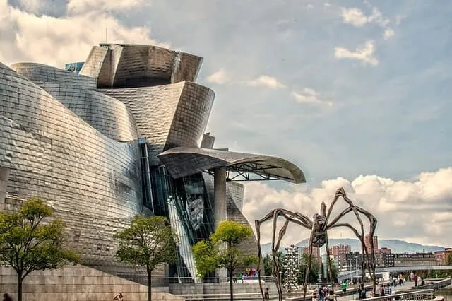 angled silver structure of the Guggenheim Museum in Bilbao Spain next to the long legged spider like iron sculpture