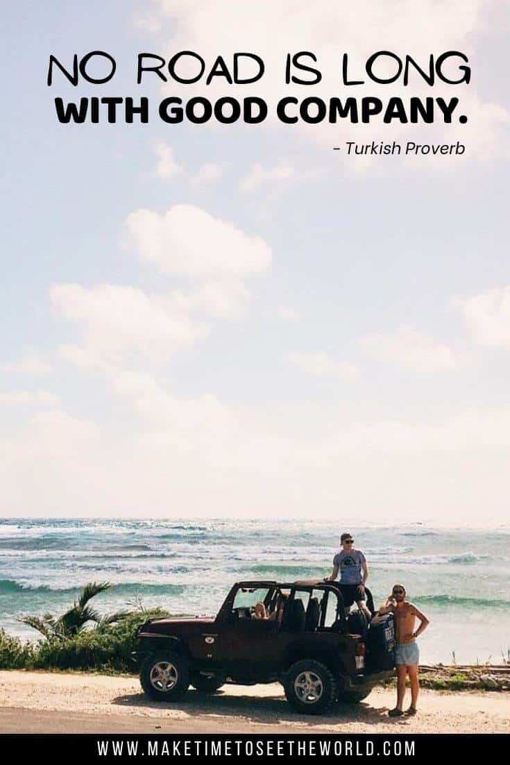 An open top jeep parked at the side of the road in front of the ocean with one guy standing in the car and one next to it with text overlay No road is long with good company